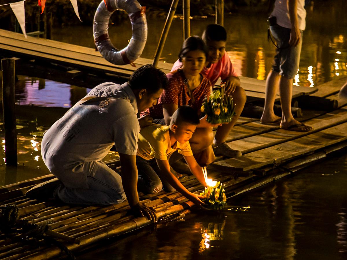 People placing candle-lit krathongs on the Ping River at night